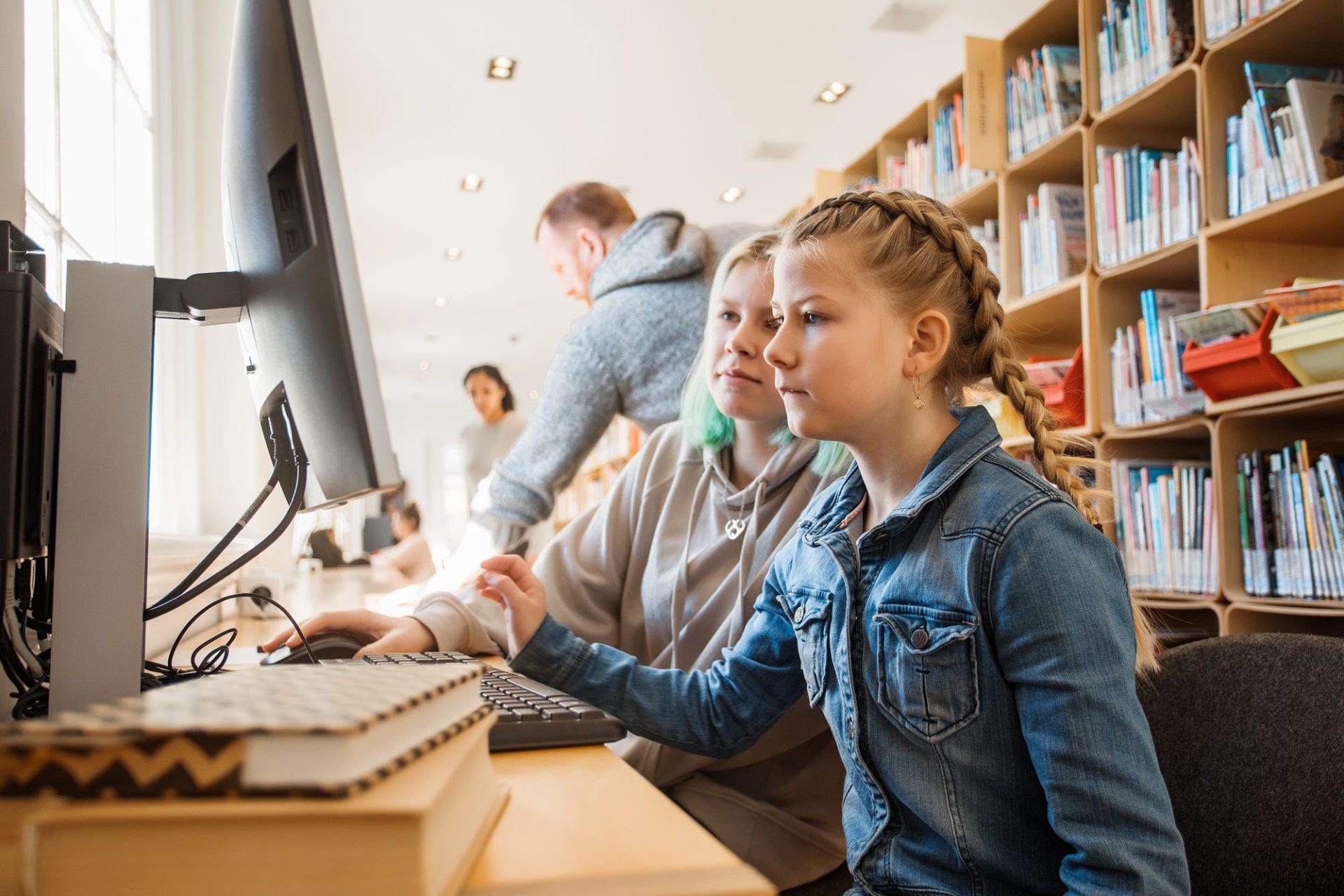 Leerlingen zoeken samen een boek op in de schoolbibliotheek